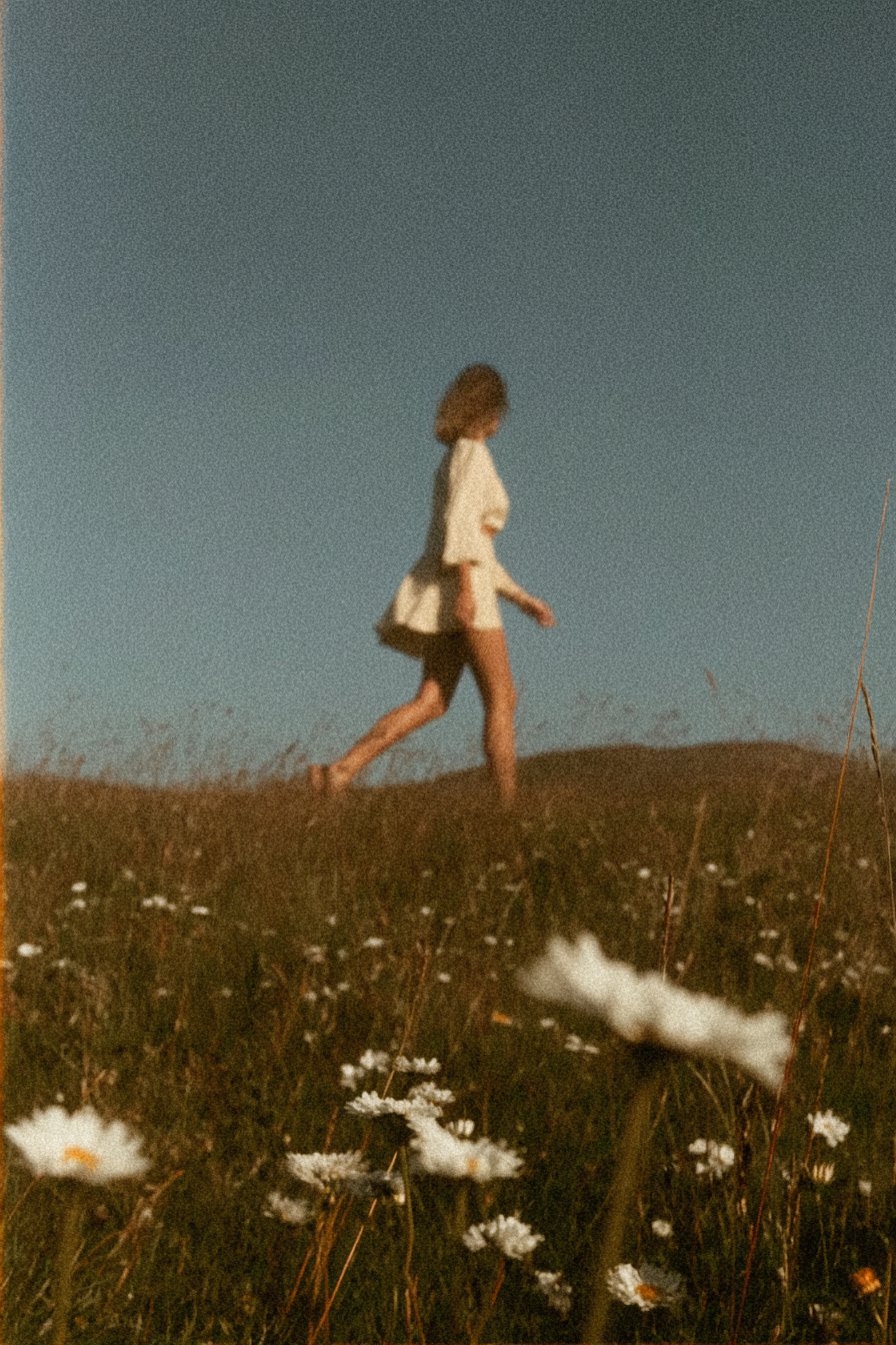 A woman walking through a meadow of daisies in evening light